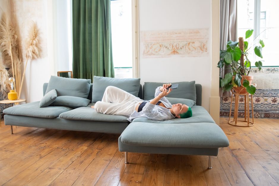 Woman with green hair lounging on a sofa using a smartphone at home