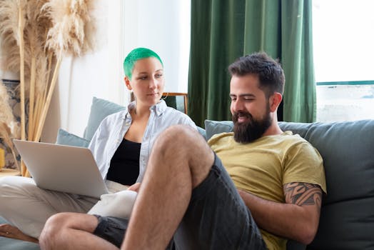 Young couple sitting on a sofa using a laptop, creating a cozy at-home atmosphere.