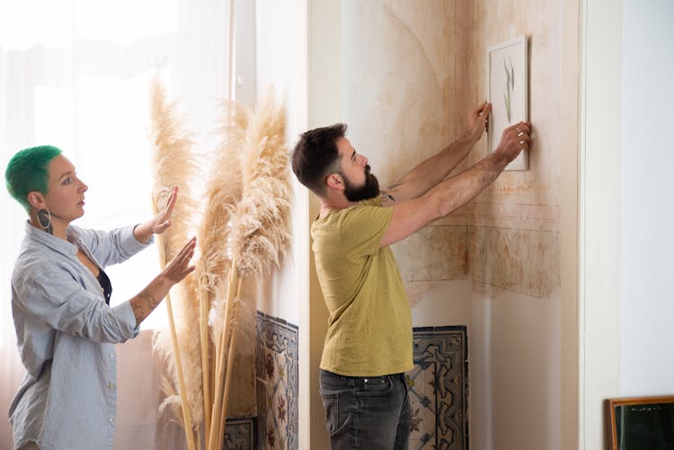 A Couple Hanging A Frame On The Wall