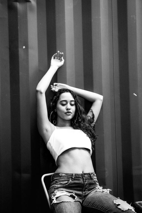 Free Black and white of young female in casual clothes sitting on chair and raised hands up while looking down Stock Photo