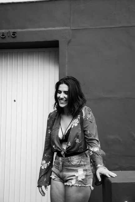 Black and white of young smiling female in trendy outfit standing near wall of building