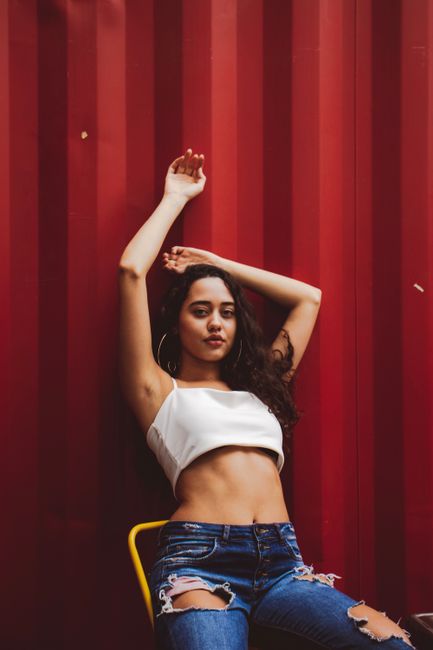 Young woman with long hair poses stylishly against a bold red backdrop.