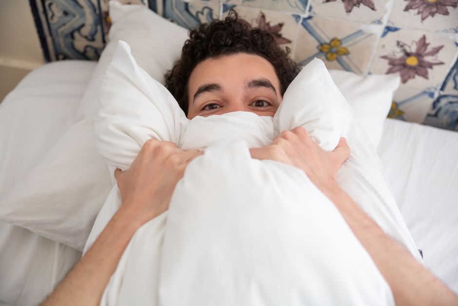 Como Lidar com o Medo de Dormir e Melhorar seu Descanso 2 A young man relaxing in bed with a pillow, enjoying a peaceful morning indoors.