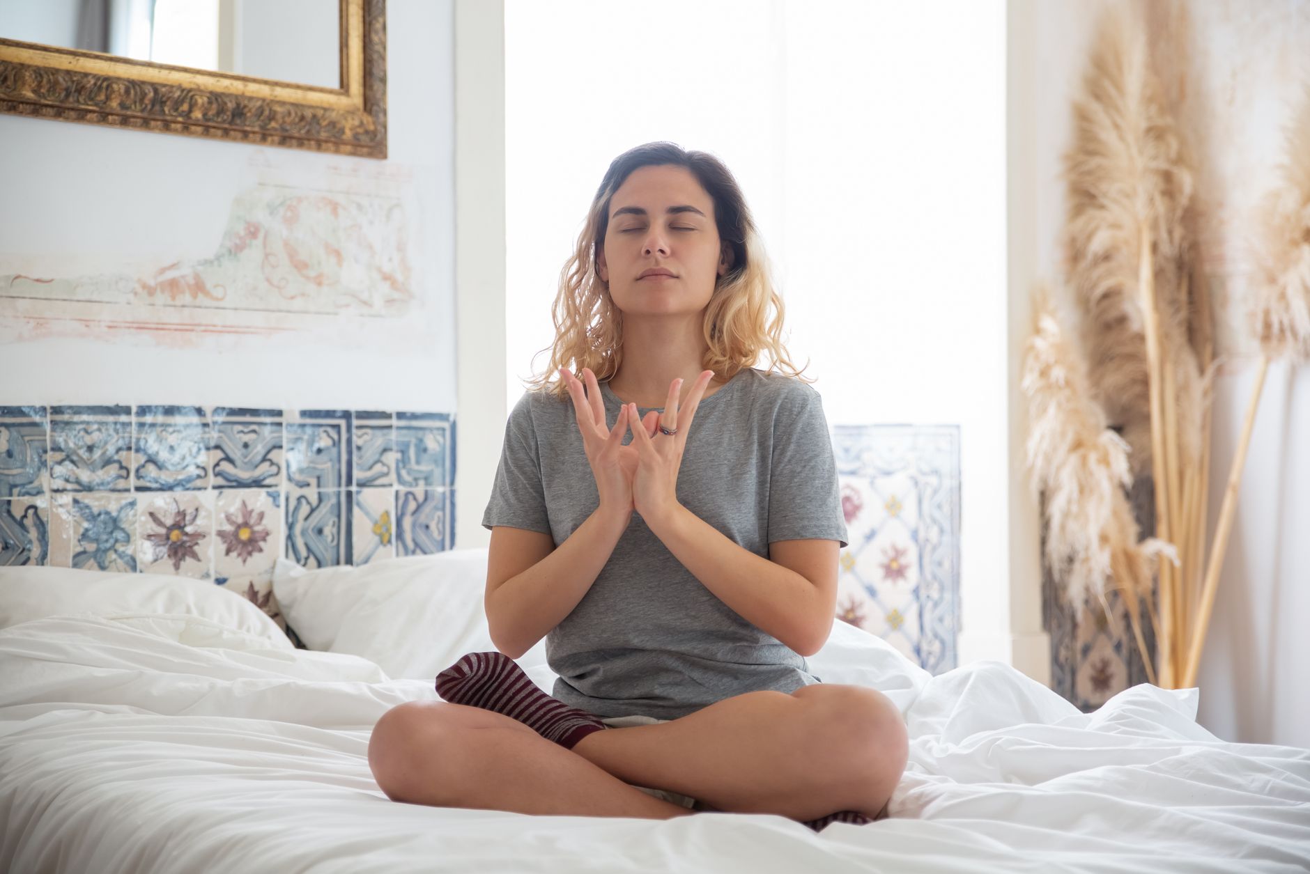 A woman meditating in a peaceful bedroom setting with soft natural light.