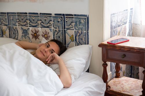Free A woman lies in bed inside a tiled bedroom in Portugal with a smartphone on a side table. Stock Photo