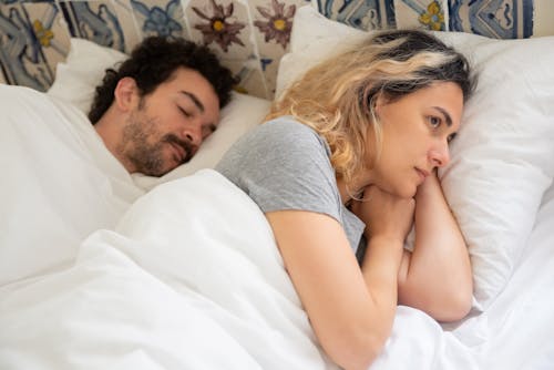 Free Woman in Gray Shirt Lying on the Bed beside a Man Stock Photo