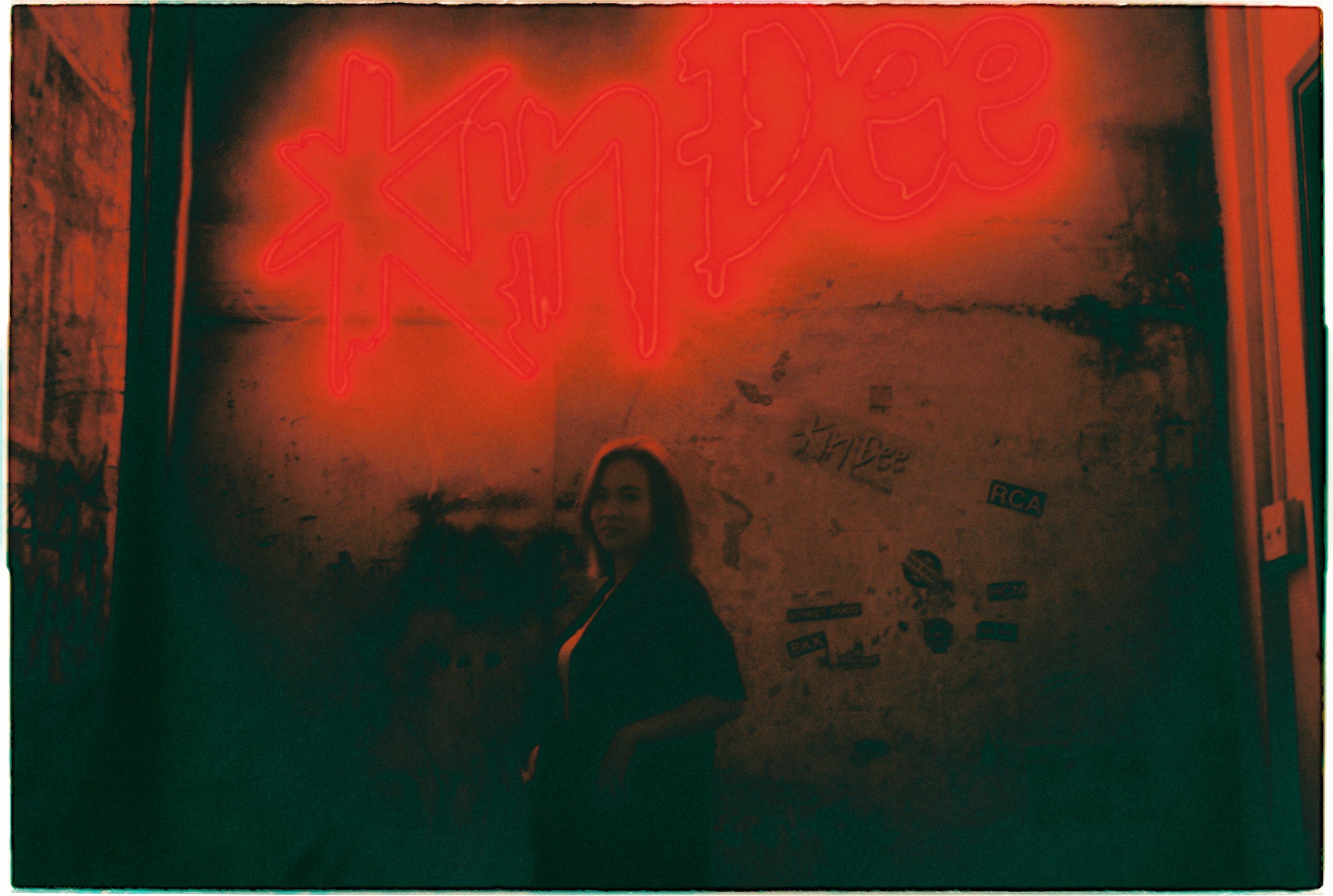 A woman silhouetted against vibrant red neon signage in a dark, moody setting.