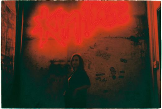 A woman silhouetted against vibrant red neon signage in a dark, moody setting.