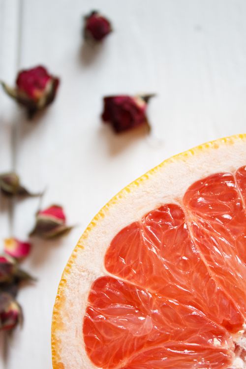 Free From above of slice of fresh juicy orange against dry buds of red roses placed on light table Stock Photo