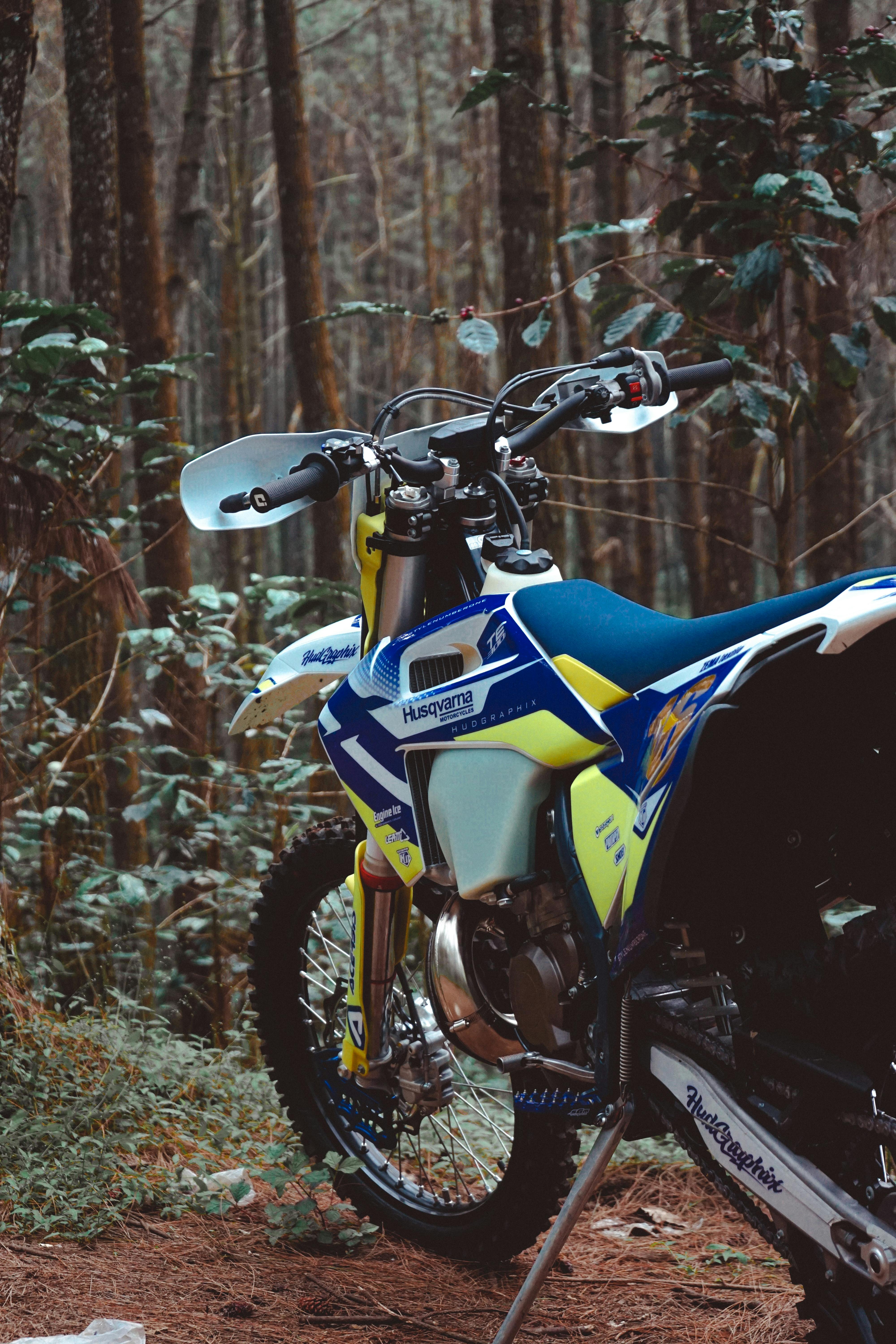 Parked blue and yellow motorcycle in a wooded forest, showcasing outdoor adventure.