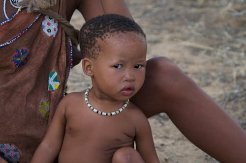 Topless Boy With Handmade Necklace Sitting Beside Woman