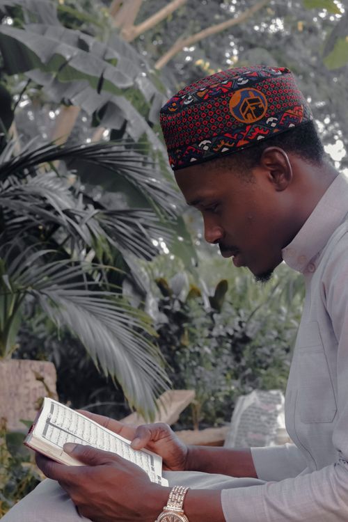 Free A man in traditional attire reads a religious book outdoors surrounded by foliage. Stock Photo