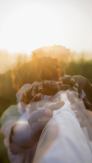 A creative double exposure photo capturing hands reaching out with blurred effects, outdoors at sunset.