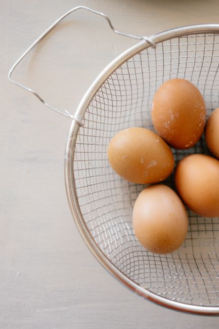 A close-up shot of fresh brown eggs in a metal wire basket on a neutral background.