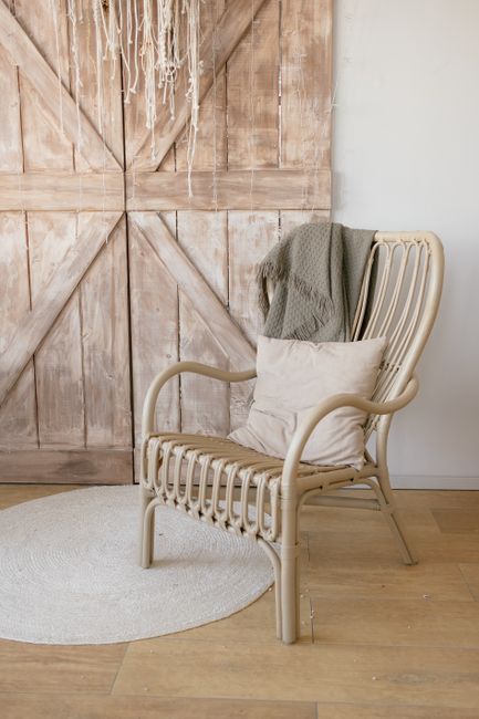 A stylish wicker armchair with pillows in a rustic interior with wooden walls and parquet floor.
