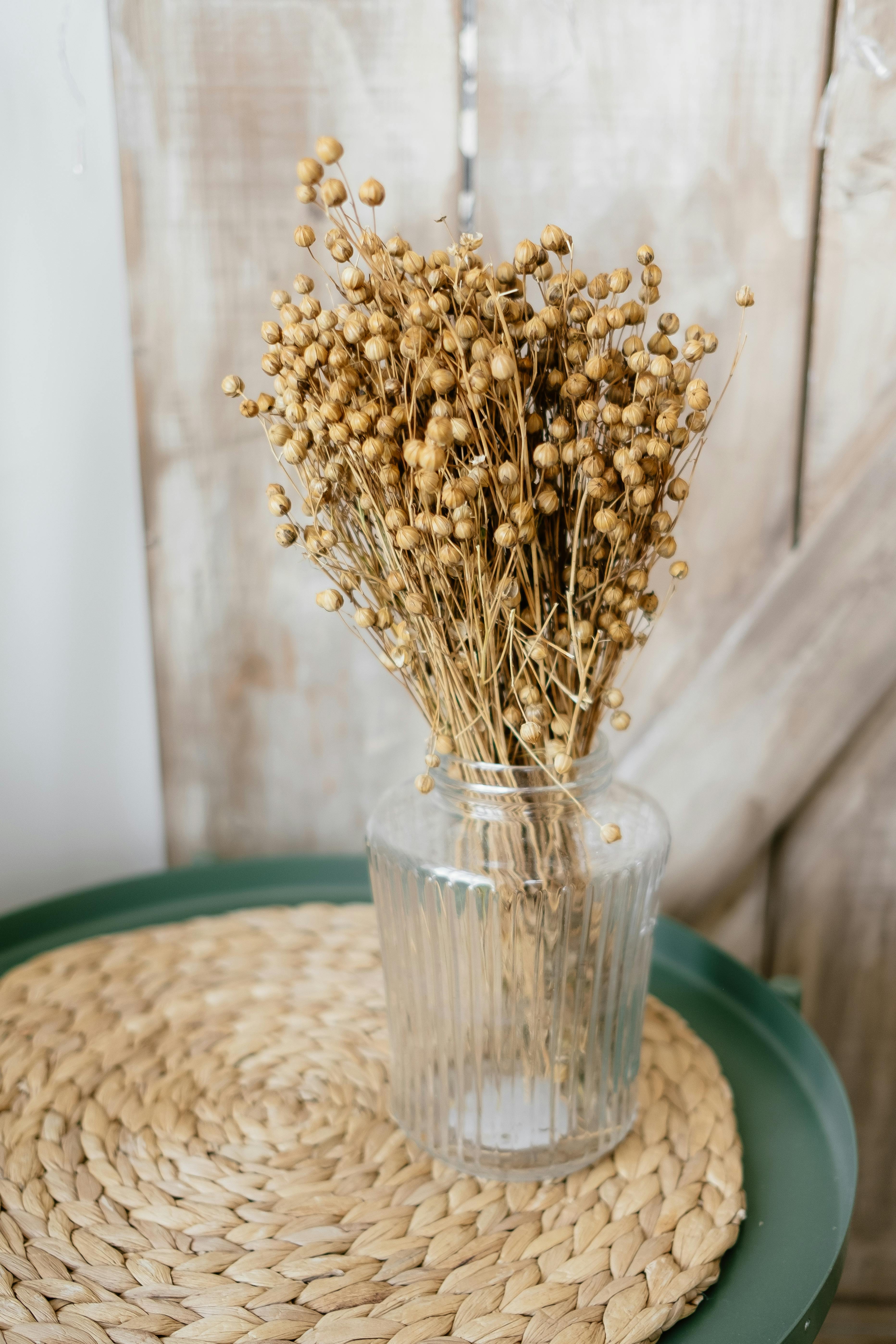 Stylish rustic decor featuring dried flowers in a glass vase on a braided mat.