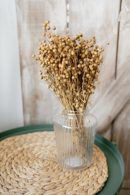 Stylish rustic decor featuring dried flowers in a glass vase on a braided mat.