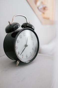 Classic black alarm clock with bells on a white table, capturing time concept.