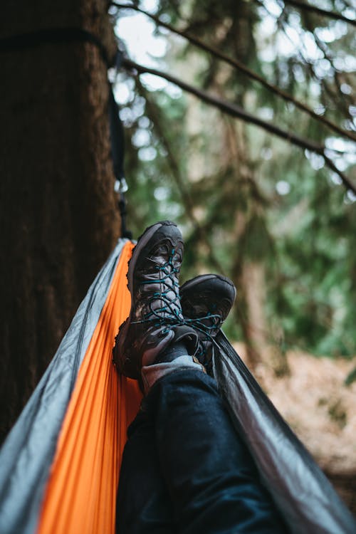 Free Person Wearing Pair of Black Hiking Shoes Lying on Orange and Gray Hammock Stock Photo
