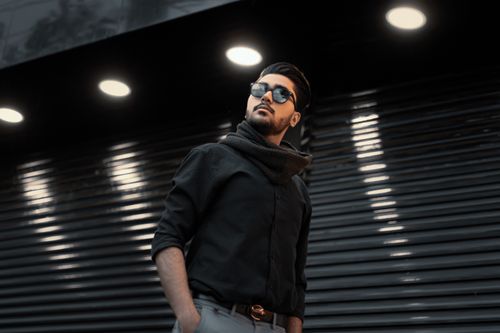 Free A fashionable man in sunglasses with a scarf poses under spotlights in an urban setting. Stock Photo