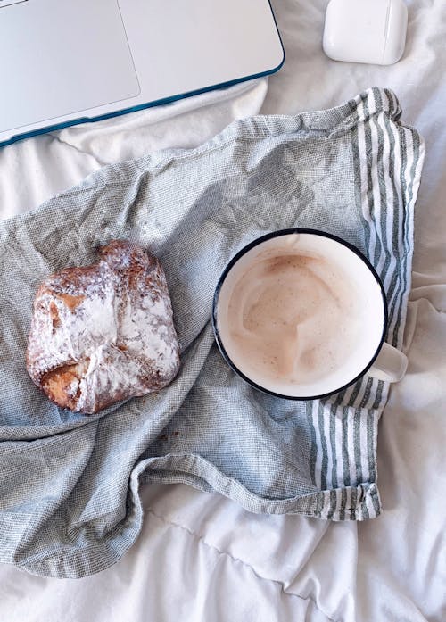 Free Top view of delicious sweet pastry with powdered sugar placed near mug of coffee and laptop with earbuds in case Stock Photo