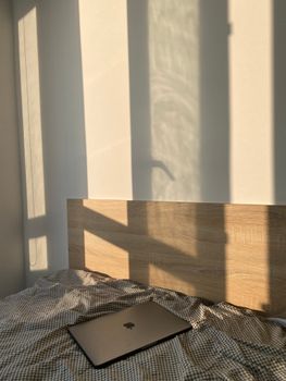 A cozy bedroom with soft sunlight casting shadows and a laptop on the bed.