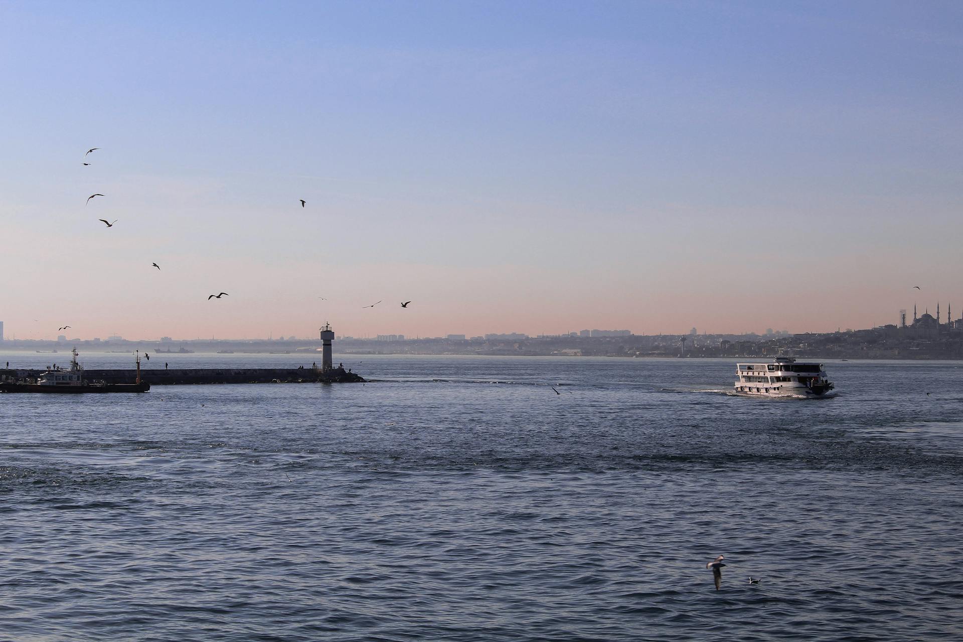 A tranquil coastal scene featuring a ferry and lighthouse at sea under a clear sky.