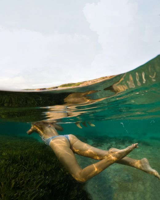 Underwater view of a woman swimming in clear tropical waters near a coast.