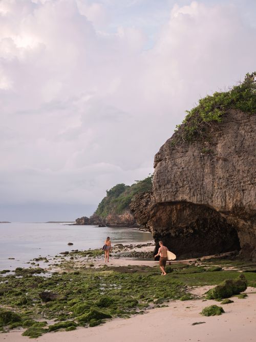 Free Two surfers walk along a scenic moss-covered beach with dramatic cliffs, embracing the coastal adventure. Stock Photo