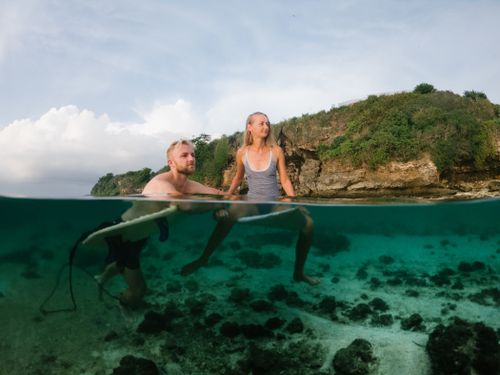 Free Caucasian couple enjoys a sunny day surfing by the tropical shoreline, half-submerged in water. Stock Photo