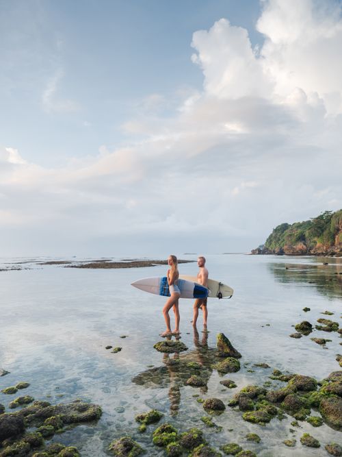 Free A couple with surfboards explores a scenic rocky beach at dawn. Stock Photo