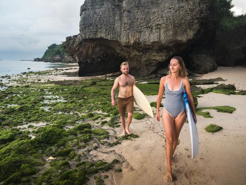 Free Two adults enjoy a seaside adventure with surfboards on a rocky tropical beach. Stock Photo