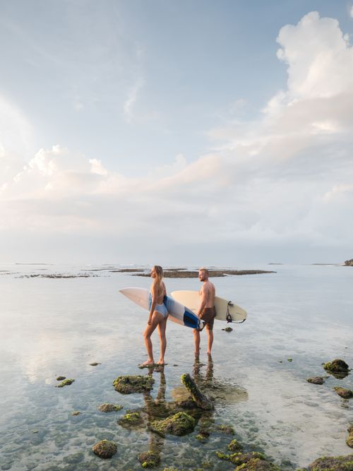 Free Surfers standing on a rocky shore with surfboards under a clear sky, ready to surf. Stock Photo