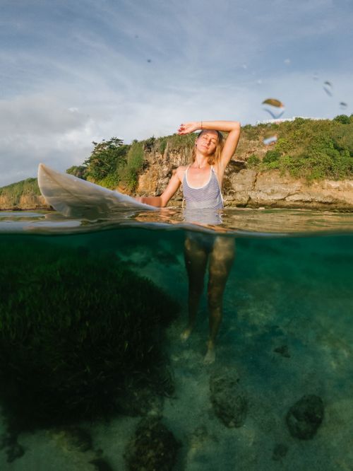 Free A female surfer standing in clear waters with a surfboard on a sunny day. Stock Photo