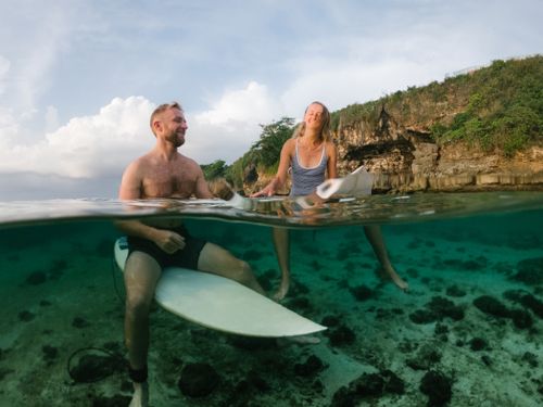 Free A man and woman enjoying leisure time on surfboards in clear tropical waters with a rocky shoreline. Stock Photo