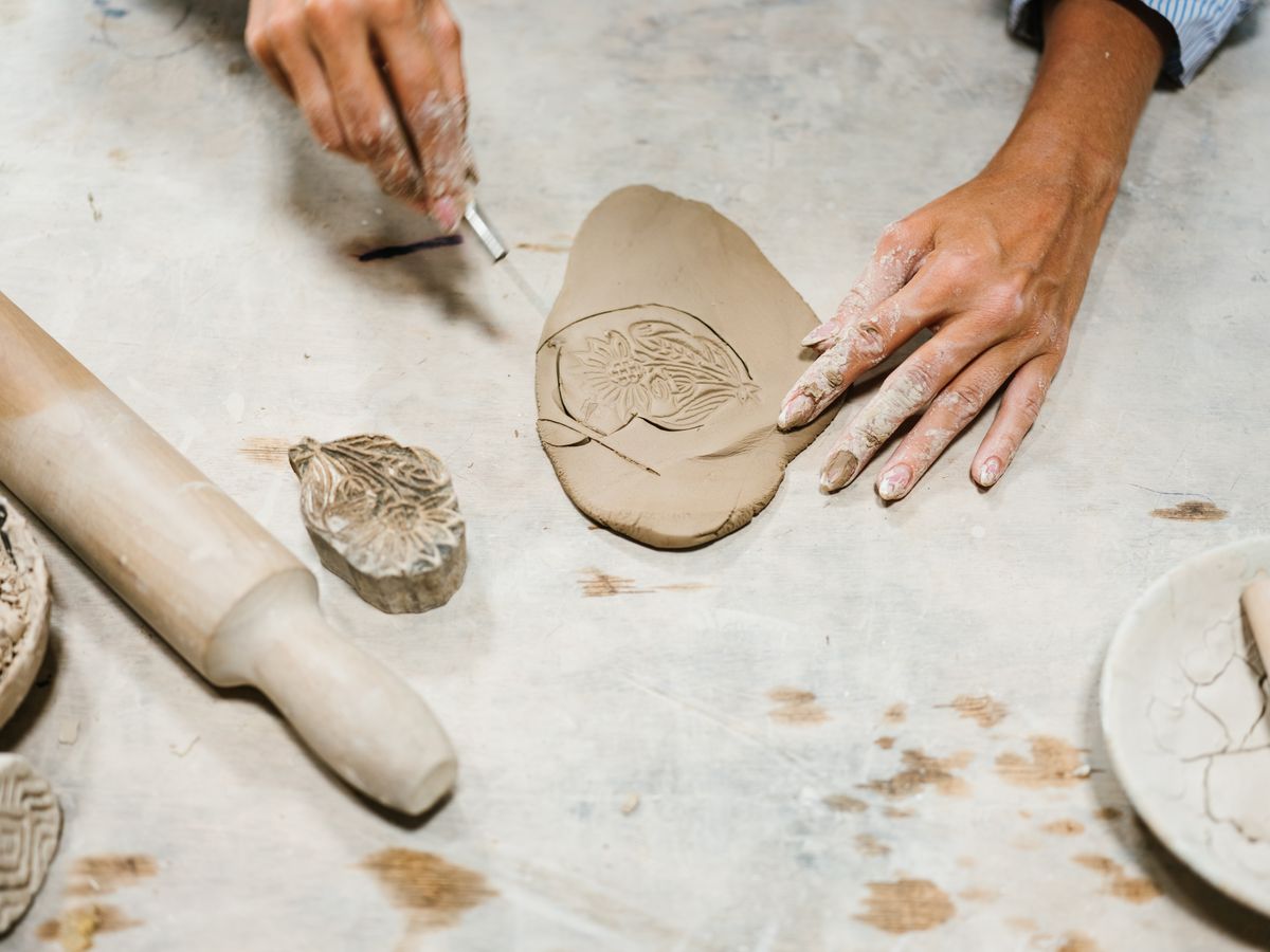 Hands stamping a detailed pattern into soft clay for a personalized name plaque