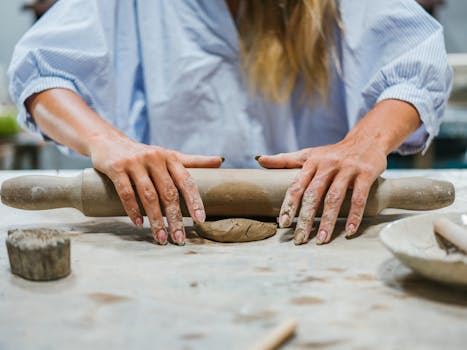 Hands shaping clay with a rolling pin during a pottery session.