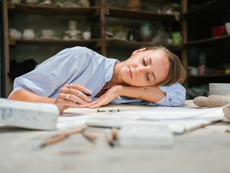 Artist Lying On Workbench Idly Playing With Her Tools