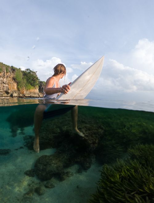 Free Over-under shot of a woman with a surfboard sitting in clear tropical waters, showcasing the vibrant marine life. Stock Photo