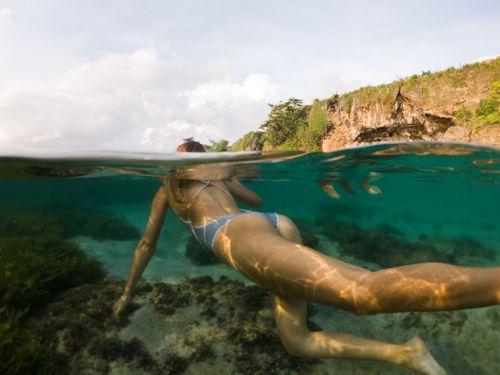 Free Woman snorkeling in clear tropical waters near rocky coastline. Stock Photo