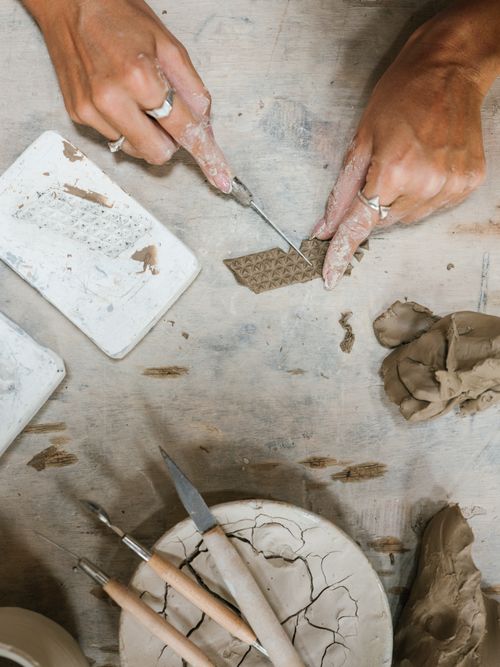 Free Top view of hands crafting pottery using clay tools on a wooden surface, depicting creativity and skill. Stock Photo