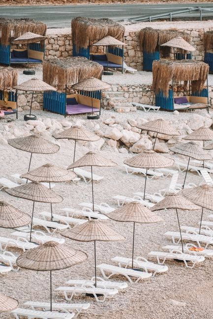 Aerial beach view in Antalya with aligned sunbeds and straw umbrellas on a pebble coast.