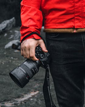 Photographer holding a DSLR camera wearing a red jacket in an outdoor setting. Ideal for stock photo use.