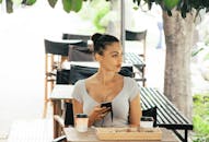 咖啡馆外，一名女子坐在桌边，手里拿着手机，桌上放着咖啡