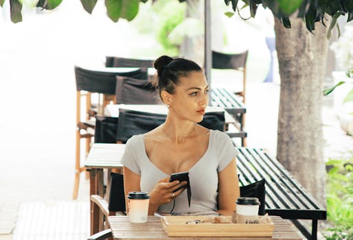 咖啡馆外，一名女子坐在桌边，手里拿着手机，桌上放着咖啡