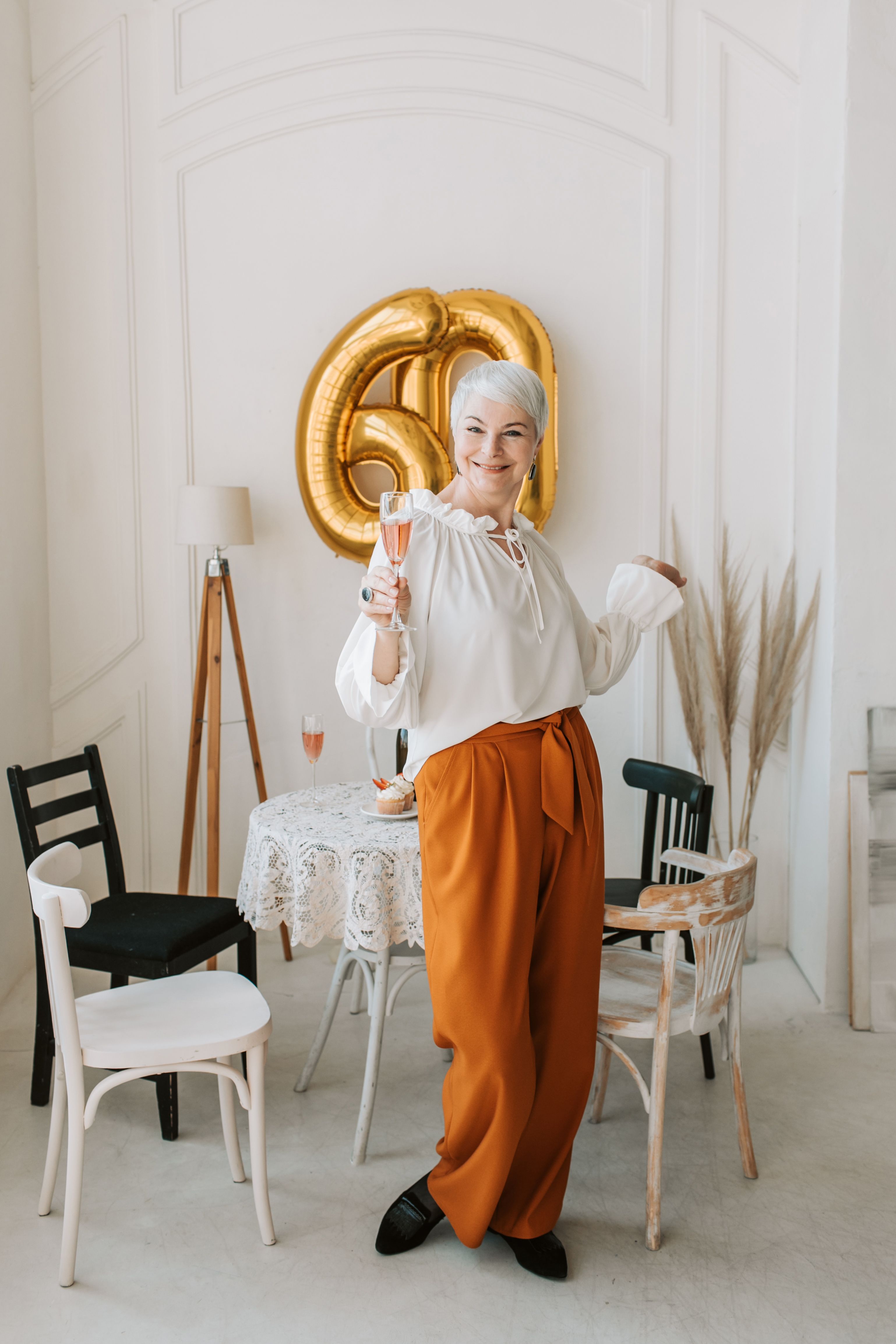 Elderly woman joyfully celebrating her 60th birthday indoors with champagne.