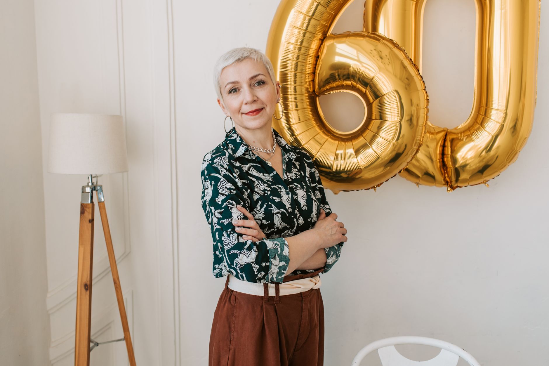 Stylish senior woman posing indoors with 60th birthday balloons, exuding grace and confidence.