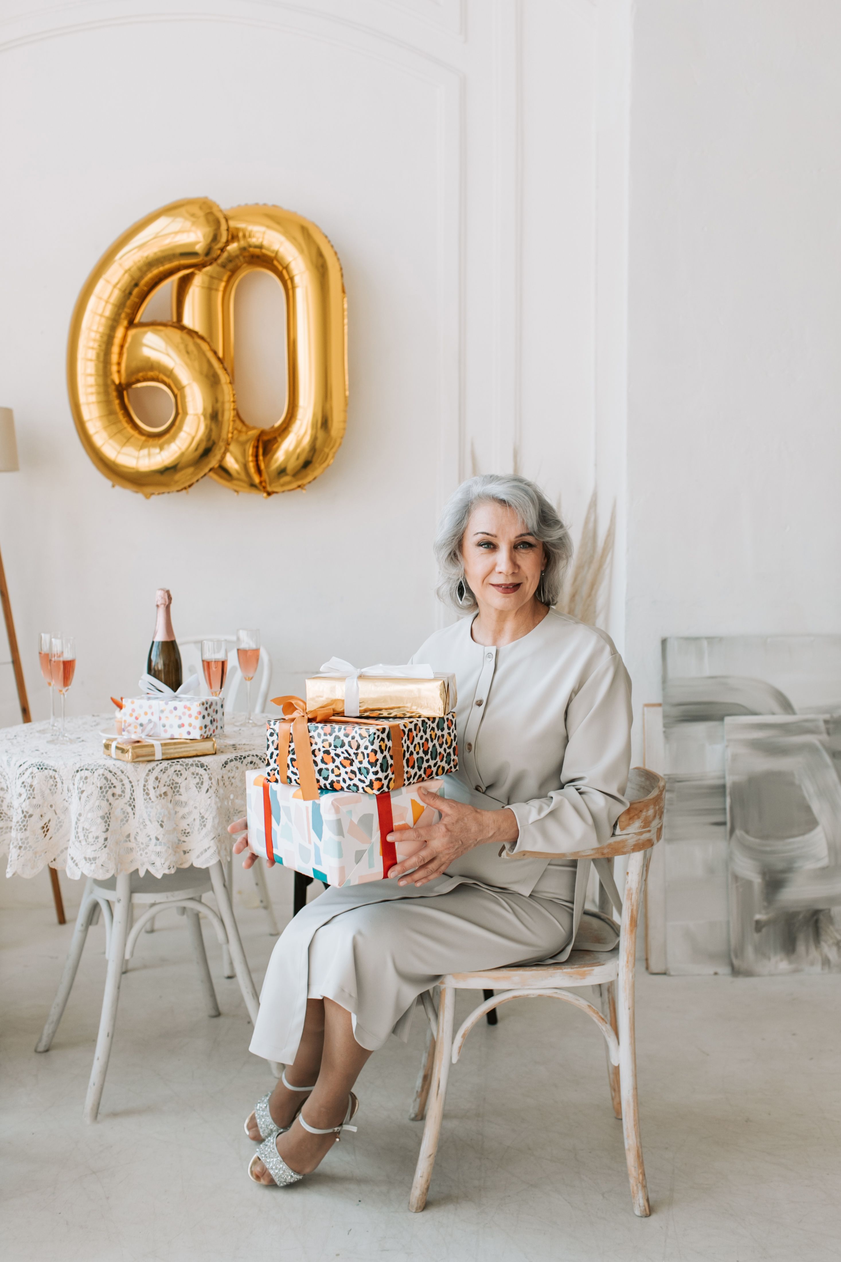 A sophisticated senior woman celebrates her 60th birthday with gifts and champagne in a stylish setting.
