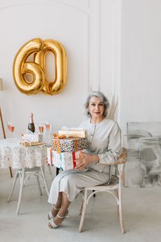 A sophisticated senior woman celebrates her 60th birthday with gifts and champagne in a stylish setting.