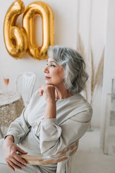 A graceful senior woman seated indoors, reflecting on her 60th birthday with champagne.